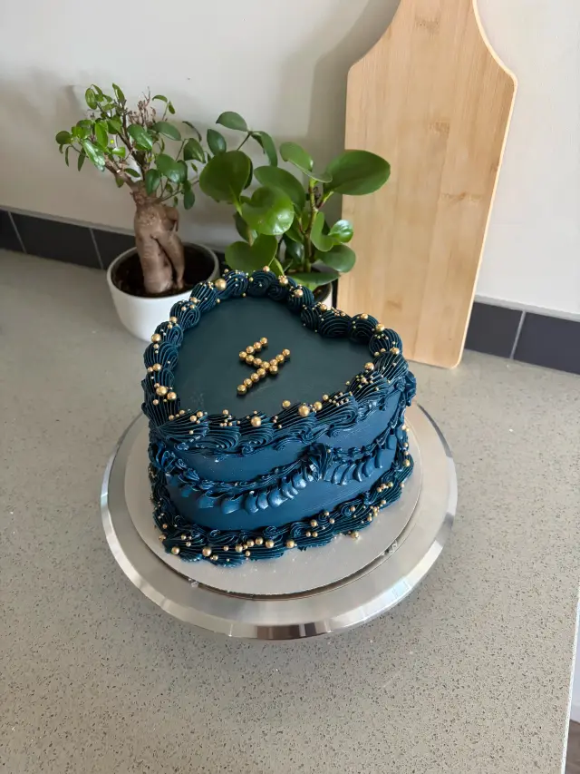 Deep navy heart-shaped cake with matching piped vintage swirls, scattered gold sugar pearls, and a number four spelled out in gold pearls.