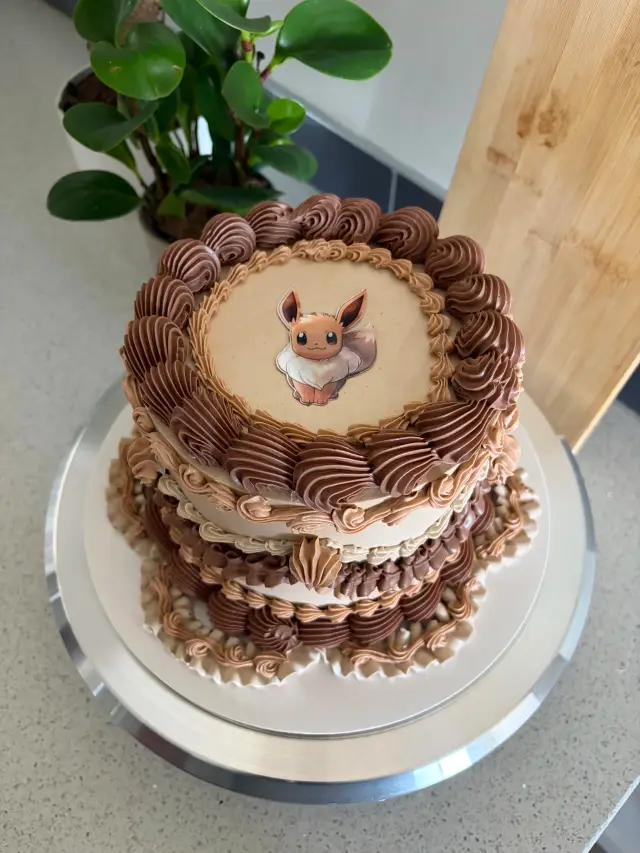 Chocolate cake layered with piped brown and cream ruffles, topped with a round character disc.