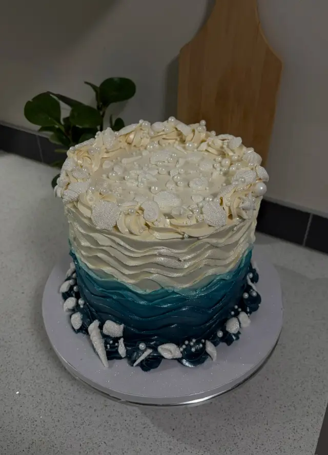 Cake with a crown of white ruffled buttercream on top fading into a textured navy and white base.