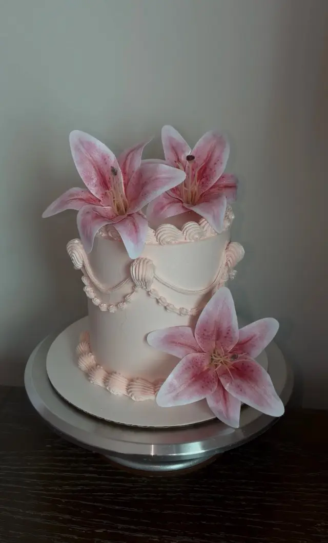 White buttercream cake with large pink sugar lilies and a trail of pearls running down one side.