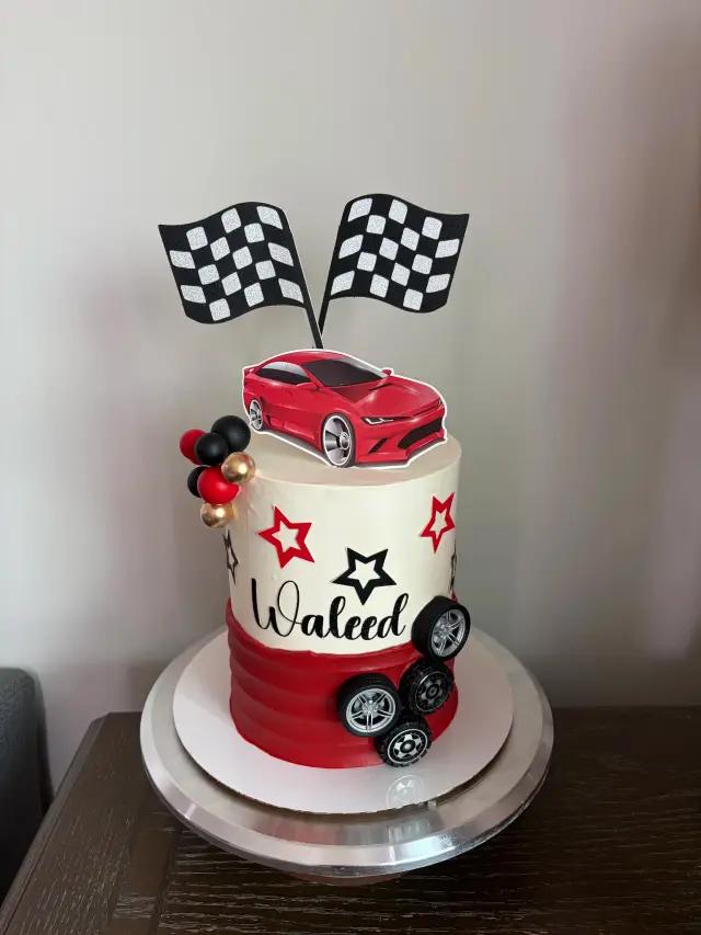 Red and white cake with a fondant race car, chequered racing flags and wheels around the base.
