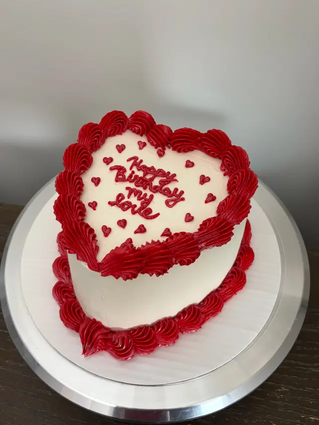 Heart-shaped cake piped with red rosettes and small hearts on white buttercream, with Happy Birthday written in the centre.